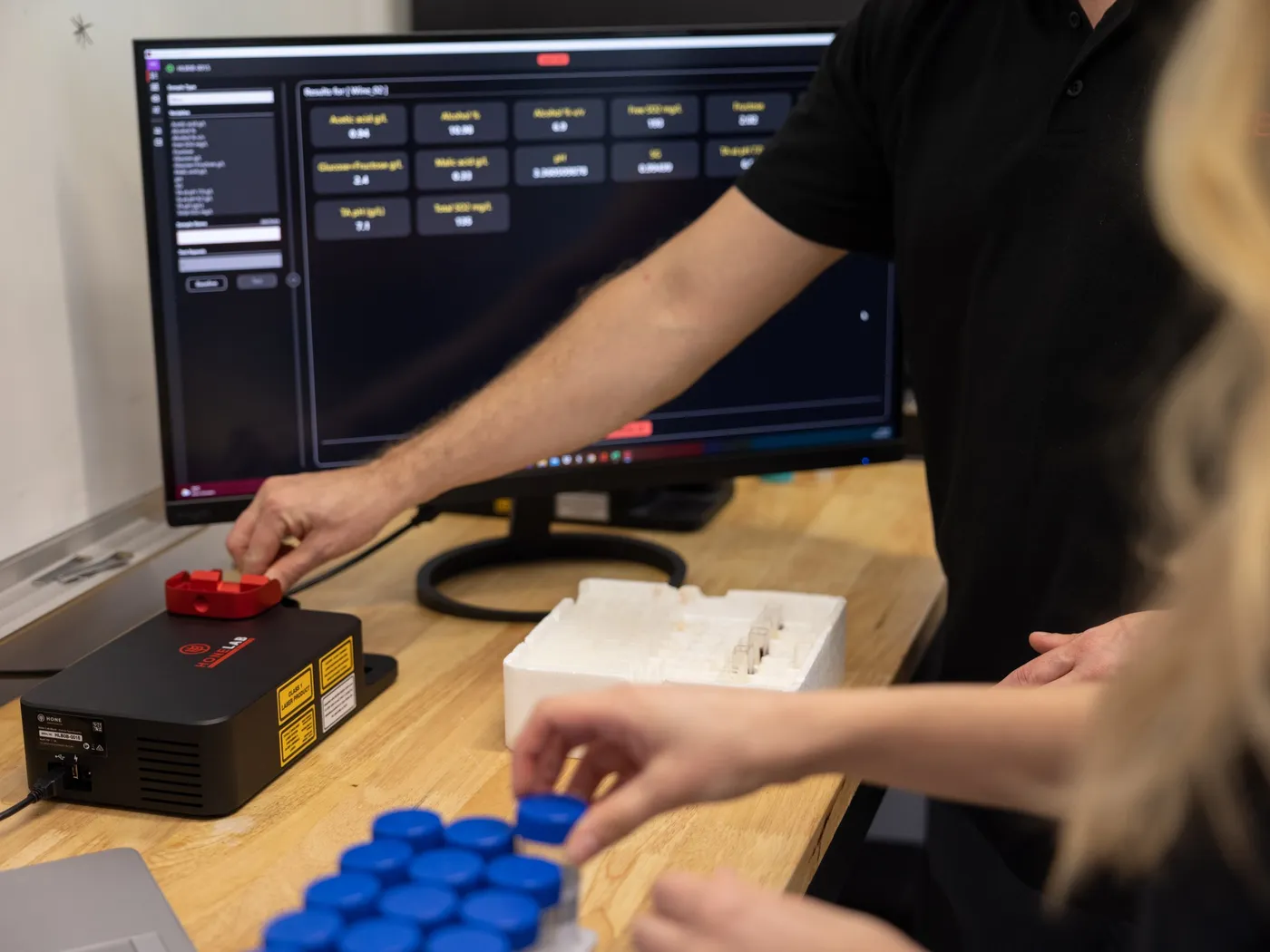 A Hone Lab Black on the bench with results on screen, a hand reaching for a sample vial