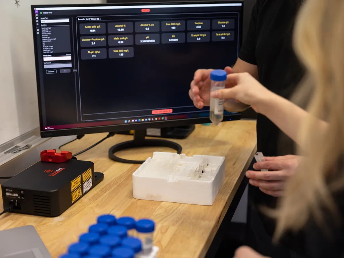 A Hone analyst placing a sample vial in the Lab Black, with results on the screen behind
