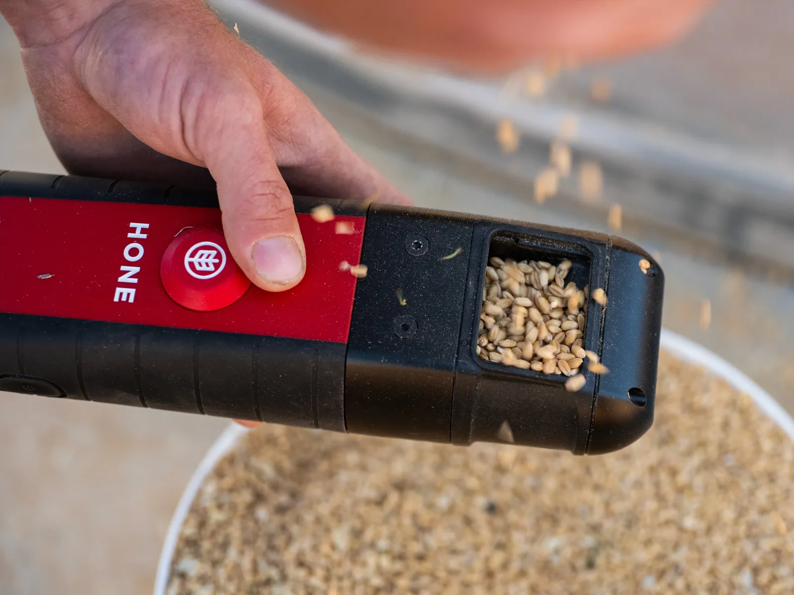 A thumb on the red button of the Hone Lab Red as grain pours into the sample window
